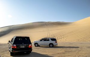 Voiture de location roulant sur une route désertique à Oman, entourée de montagnes et de paysages arides.